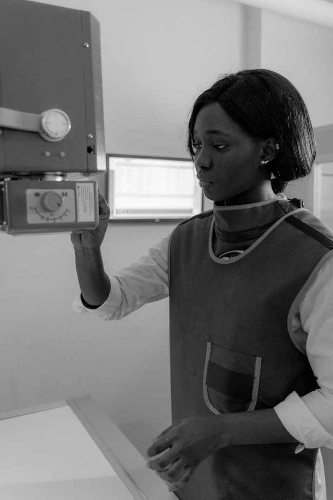 A medical professional operating an X-ray machine in a clinic setting, wearing protective gear.