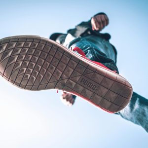 Low angle view of person wearing sneakers with focus on the sole against blue sky.